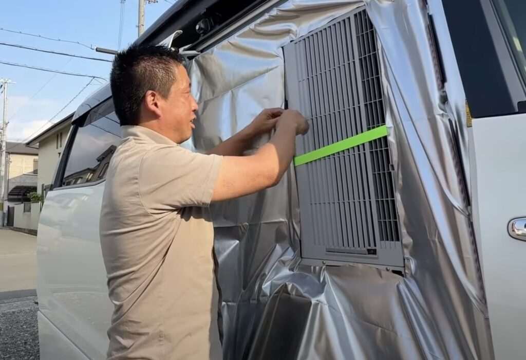 ミニバン2列目を遮光シートで覆って室外機部分だけ切り抜き露出させてるシーン