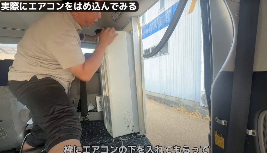 窓用エアコン本体を、車内に設置した固定枠にはめ込んでいる様子