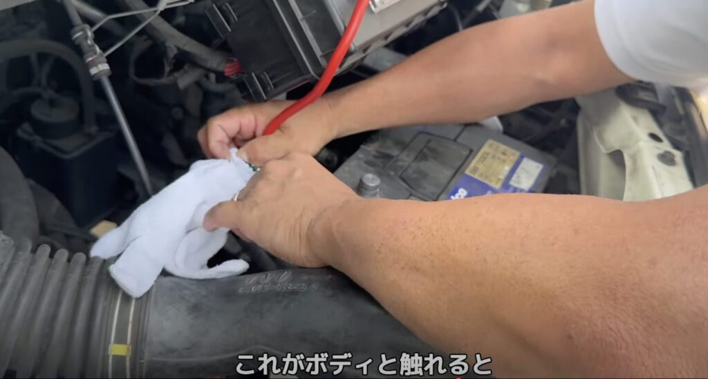 カーバッテリーの交換作業。マイナス端子からケーブルを外し、軍手で絶縁している様子
