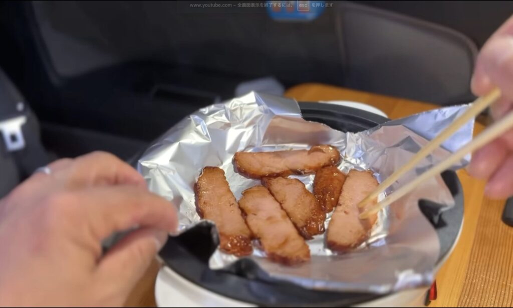車内で小型ホットプレートで焼豚を焼いている様子