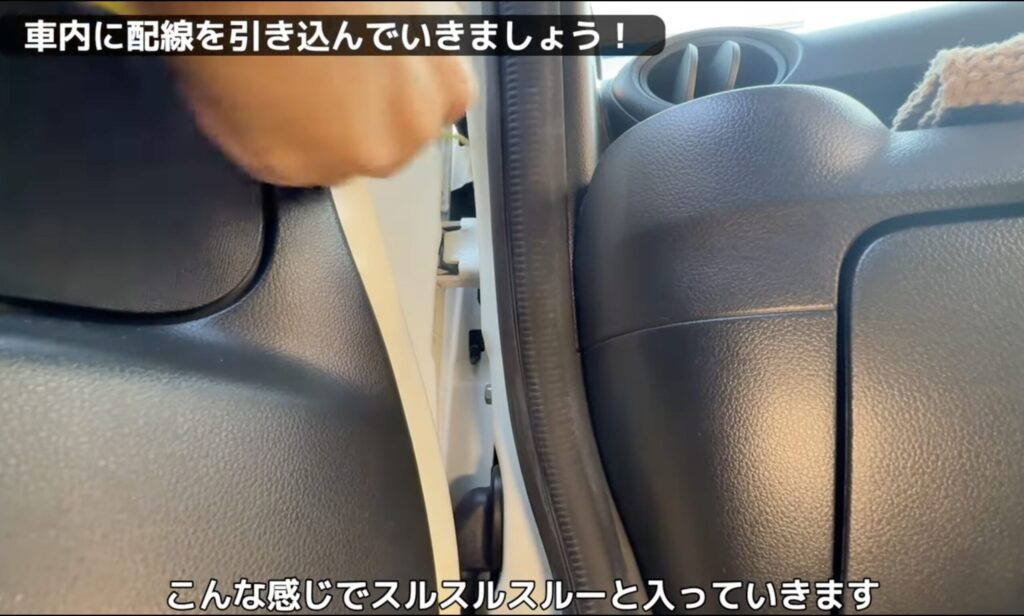 針金ハンガーをガイドにして、N-BOXの助手席側フェンダーの隙間から配線を引き込んでいる様子